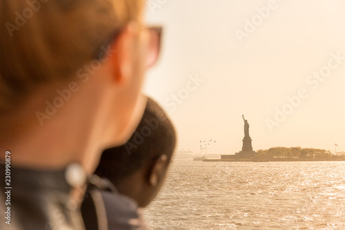 Tourists looking at Statue of Liberty silhouette in sunset from the staten island ferry, New York City, USA.