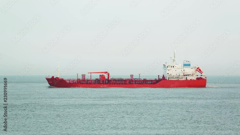 A red chemical cargo ship at sea passes before the camera. A red chemical cargo ship at sea passes before the camera.