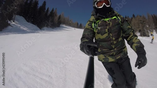 A skier with a selfie stick doing slalom skiing on the tracks in mountains and taking selfies