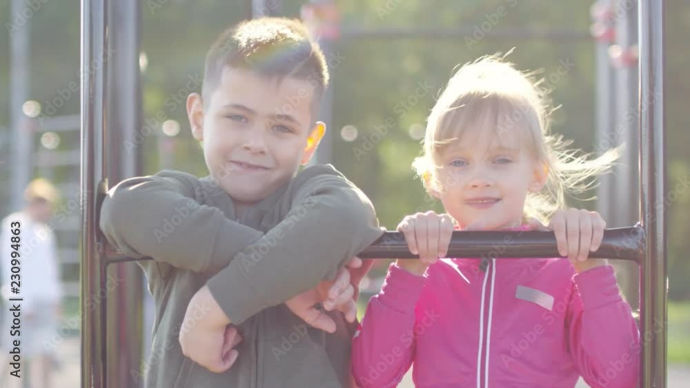 Panning shot of cute little boy and girl standing on climbing frame at outdoor jungle gym and posing for camera on sunny morning Panning shot of cute little boy and girl standing on climbing frame at outdoor jungle gym and posing for camera on sunny morning