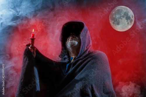 Fotografia a scary man is standing with a candle in front of a red background with moon