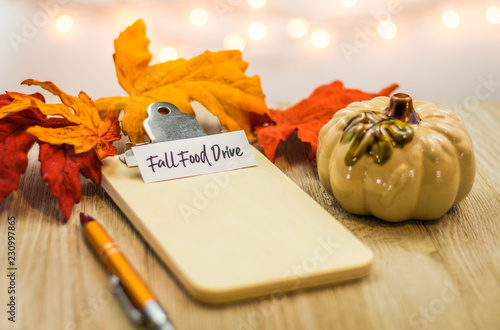 Fall Food Drive list concept on blank clipboard surrounded with bright leaves and decorative items soft background photo