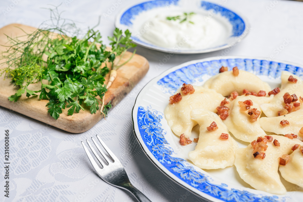 Traditional Polish dumplings with cheese and potatoes on a blue white plate. Next to cream and parsley on a wooden board.
