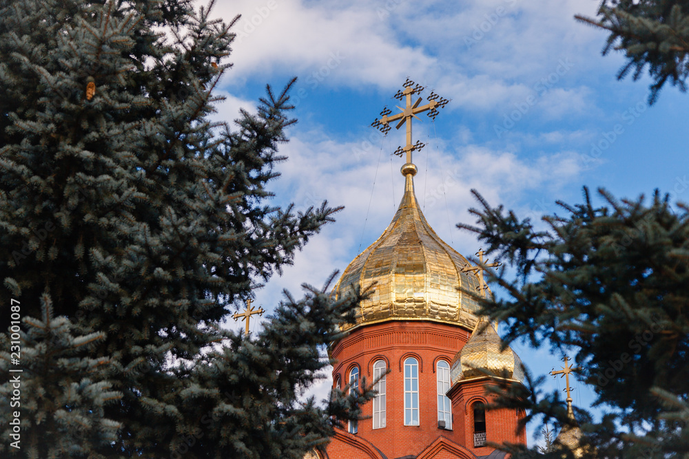 Old red brick Christian church with golden and gilded domes against a blue sky and tree branches. Concept faith in god, orthodoxy, prayer Old red brick Christian church with golden and gilded domes against a blue sky and tree branches. Concept faith in god, orthodoxy, prayer