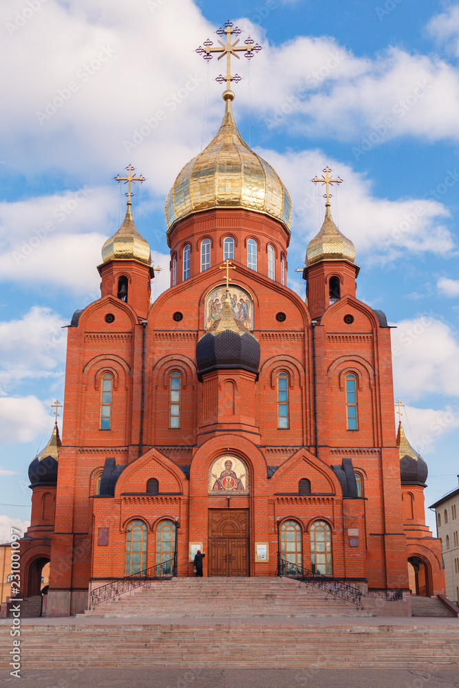 The old Russian Christian church of red brick with gold and gilded domes against the blue sky and the grandmother parishioner who came to pray. Сoncept of faith in God, orthodoxy, prayer