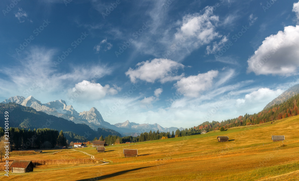 wonderful picturesque Scene in Bavarian alps. Alpine valley with wooden huts and Zugspitze on background. Amazing Alpine highland with blue sky with clouds under sunlight. Awesome nature background. wonderful picturesque Scene in Bavarian alps. Alpine valley with wooden huts and Zugspitze on background. Amazing Alpine highland with blue sky with clouds under sunlight. Awesome nature background.
