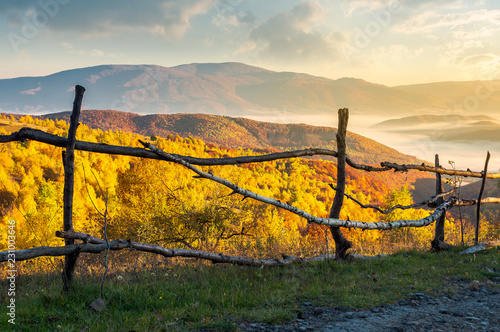 fence on the country road at sunrise. beautiful autumn scenery at sunrise. forest in golden foliage and fog in the distant valley 