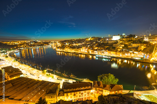 Rabelo and tourist boats on Douro River. Porto colorful nightlife of Oporto skyline and Ribeira Waterfront from Dom Luis I Bridge at night. Picturesque urban cityscape of Porto in Portugal.