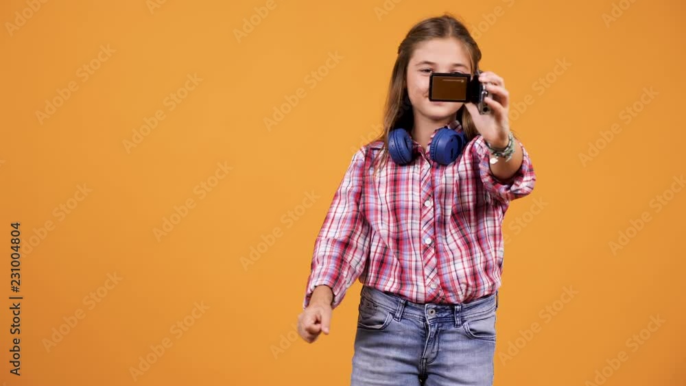 Young girl vlogging with a small camera in studio over an yellow orange background Young girl vlogging with a small camera in studio over an yellow orange background