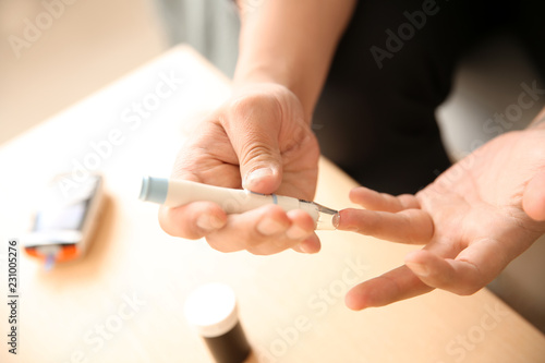 Diabetic man taking blood sample with lancet pen at home, closeup photo