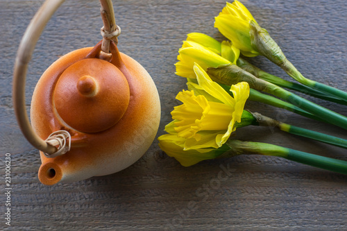 Fototapeta Naklejka Na Ścianę i Meble -  One brown teapot with several yellow narcissus on the wooden background