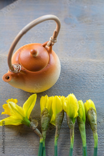 Fototapeta Naklejka Na Ścianę i Meble -  One little brown teapot with several yellow narcissus on the wooden background