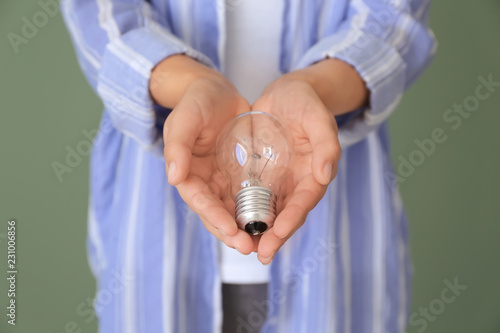 Woman with eco light bulb on color background, closeup