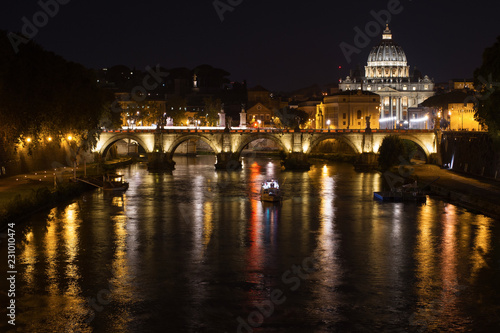 A fabulous view of night Rome with a church, a bridge, a ship and the light of lanterns reflected in the Tiber River.
