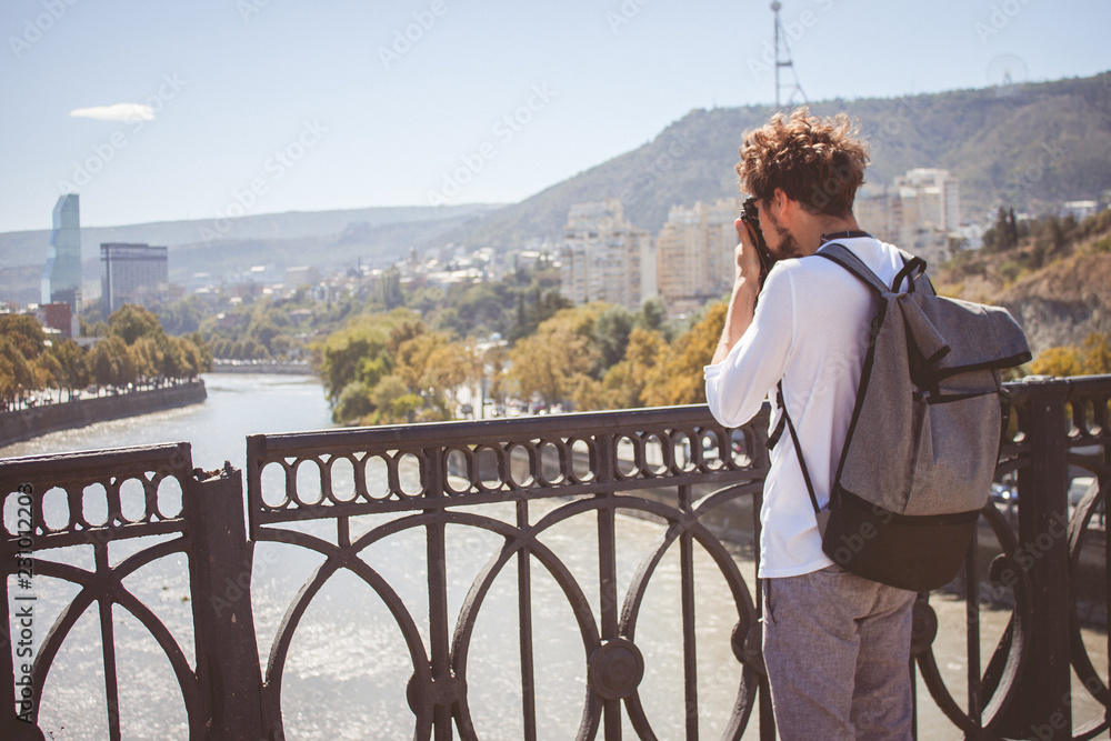 Young curly traveler taking photo with camera in Tbilisi, Georgia.