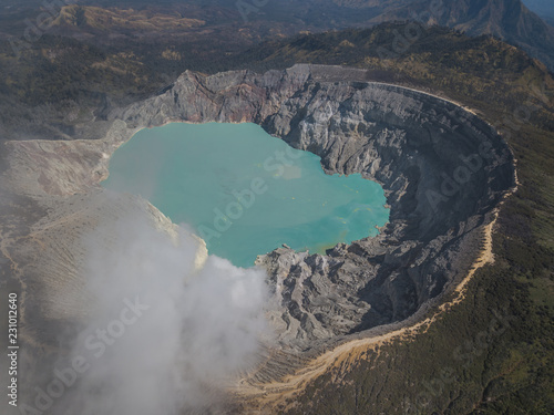 Drone shot of the Mount Ijen volcano emitting smoke from the sulfur mines and emerald sulfur lake