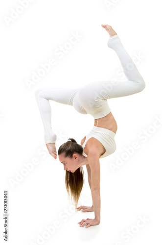 A young woman in a white suit performs acrobatic elements and yoga.