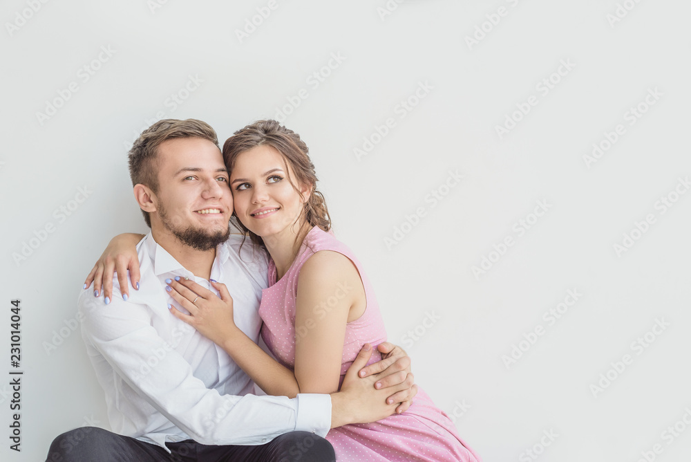 a couple in love, beautiful young people, a guy and a girl look into the distance and hugging, against the white wall a couple in love, beautiful young people, a guy and a girl look into the distance and hugging, against the white wall