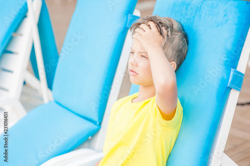 Little boy on the beach with a sunstroke touches his forehead, checking the temperature photo