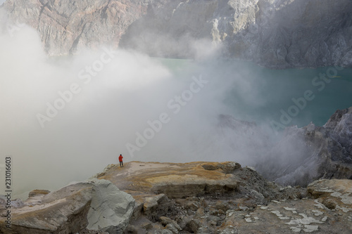 Small human standing on a rock covered in sulfur smoke inside the crater of Mount Ijen volcano in East Java, Indonesia