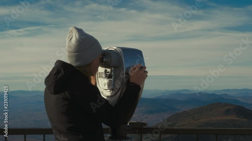 Caucasian female enjoys the view of a mountain valley through coin-operated binoculars at the viewing platform. 4K UHD