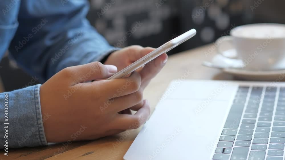 Hand of woman using smartphone on wooden table at coffee shop Hand of woman using smartphone on wooden table at coffee shop