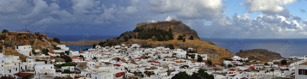 Panaroama einer weißen Stadt im Mittelmeer mit Akropolis und Meer im Hintergrund unter einem dramatischen Himmel