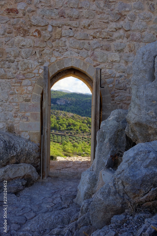 Blick durch altes Burgtor auf Olivenbäume und Weinreben