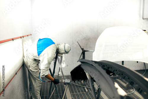 auto mechanic worker painting car bumper in paint chamber during repair work