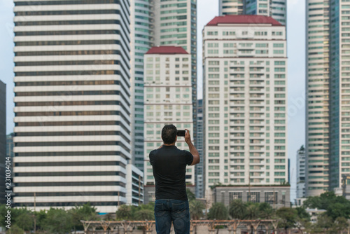 Man holding a smart phone and taking a picture with buildings in the city in background