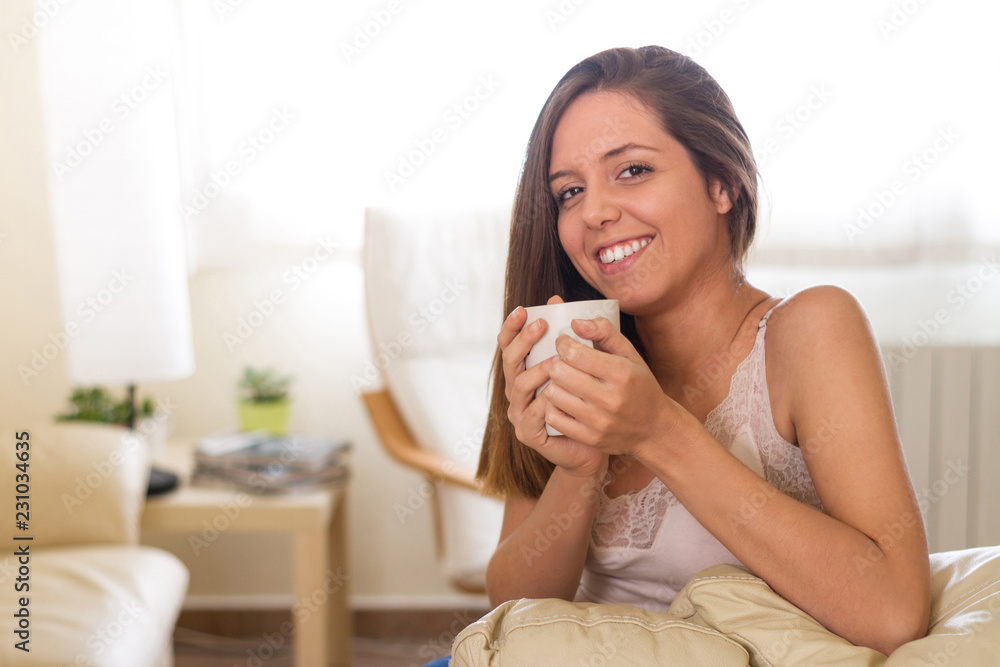 Perfect smile Young brunette laughing, happy and happy warming her hands while taking a cup of coffee or tea in living room of her house staring at the viewer Perfect smile Young brunette laughing, happy and happy warming her hands while taking a cup of coffee or tea in living room of her house staring at the viewer