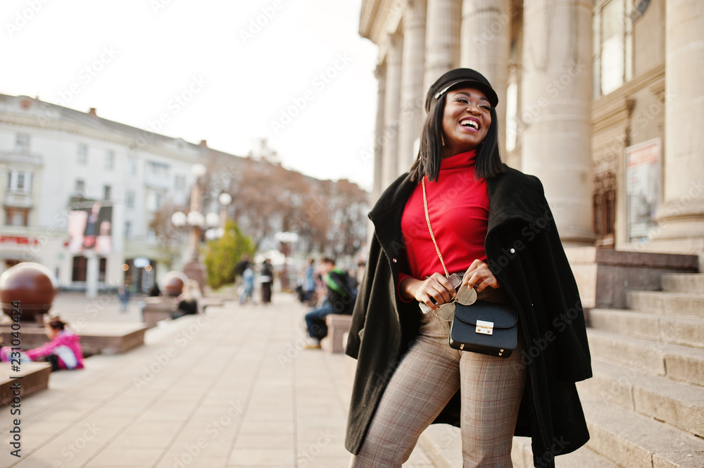 African american fashion girl in coat and newsboy cap posed at street.