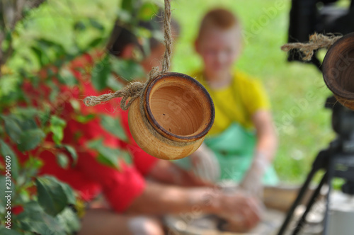 Clay pot hanging on a rope. In the background blurred Potter teaches the child to sculpt a pot on a Potter's wheel