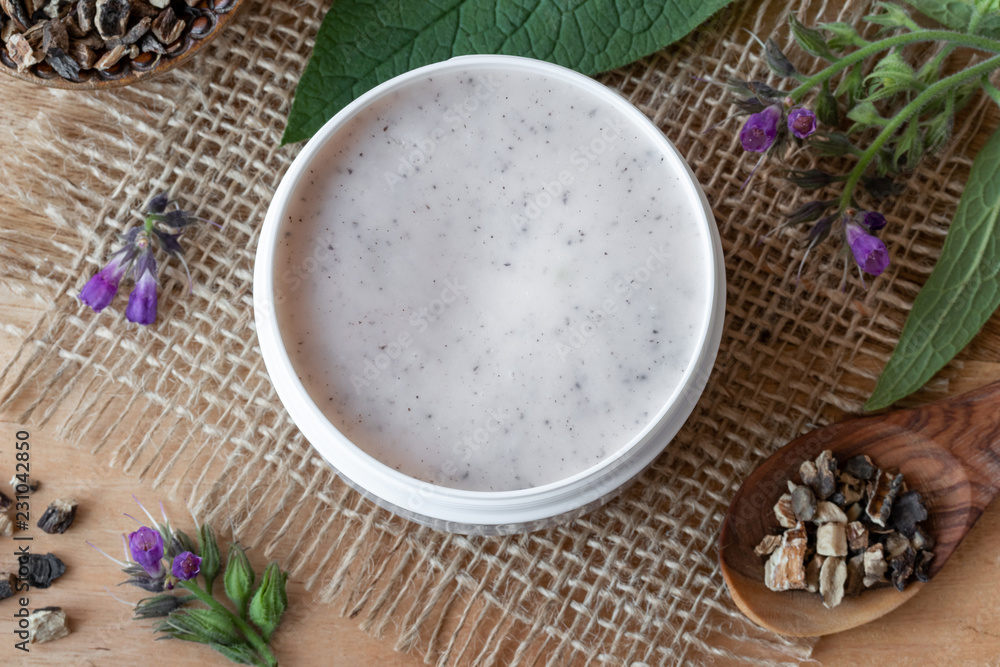 Fototapeta premium A jar of homemade comfrey root ointment with blooming comfrey plant