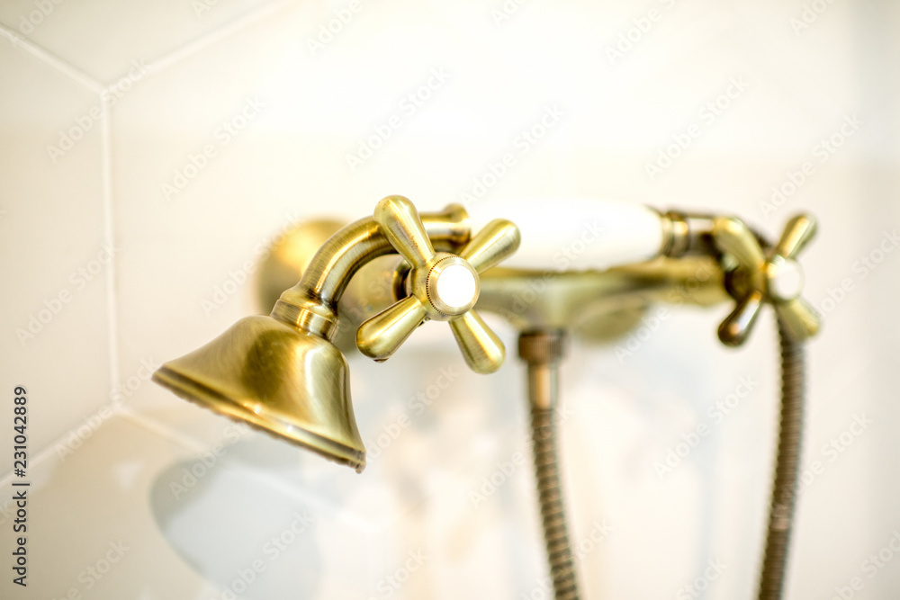 Retro style bathtub faucet made in bronze on the white tiles background, close-up view