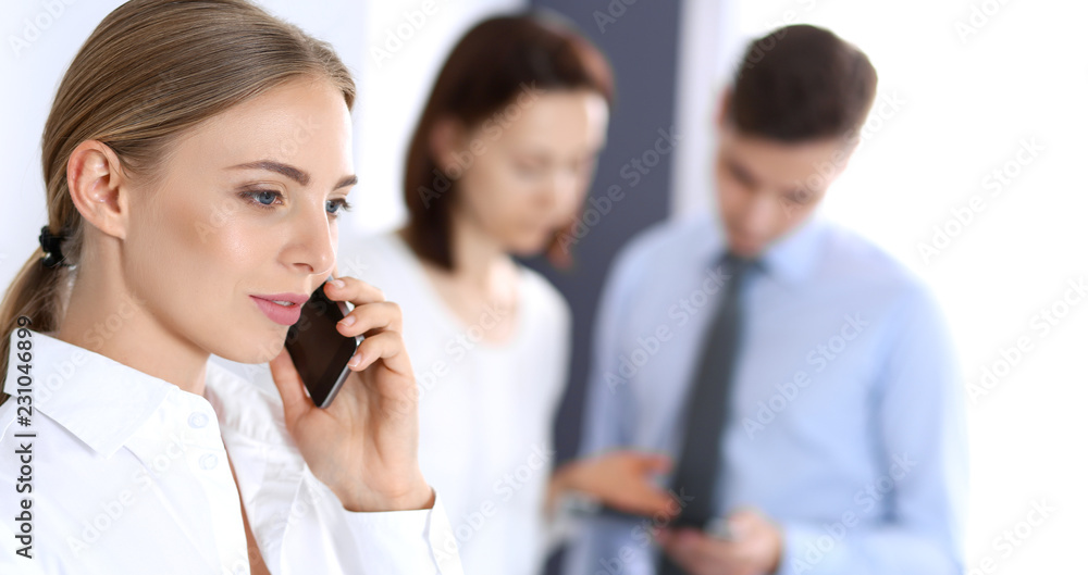 Serious blonde businesswoman talking by phone at the background of her colleagues in office. Business concept Serious blonde businesswoman talking by phone at the background of her colleagues in office. Business concept