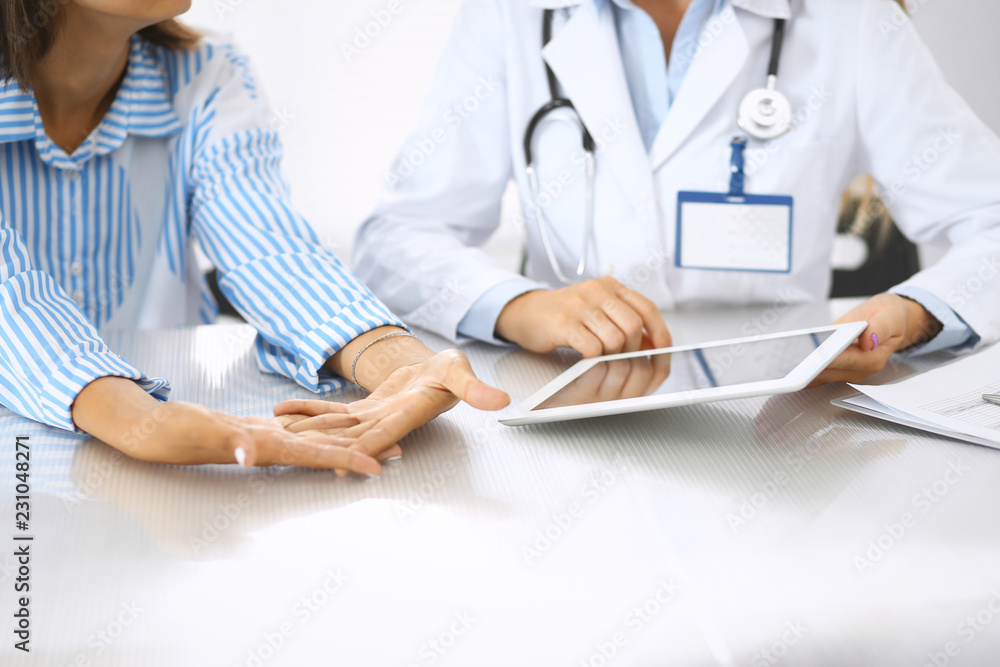 Doctor and patient talking and discussing health treatment while sitting at the desk. Physician pointing into tablet pc, close-up. Medicine and health care concept Doctor and patient talking and discussing health treatment while sitting at the desk. Physician pointing into tablet pc, close-up. Medicine and health care concept
