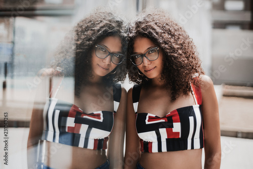 Obraz na plátně Portrait of an appealing female hipster in eyeglasses with bulky curly hair lean