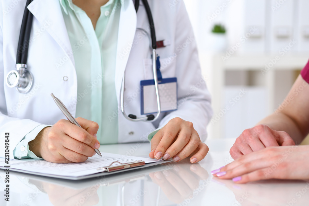 Doctor woman consulting patient while filling up an application form at the desk in hospital. Just hands close-up. Medicine and health care concept Doctor woman consulting patient while filling up an application form at the desk in hospital. Just hands close-up. Medicine and health care concept
