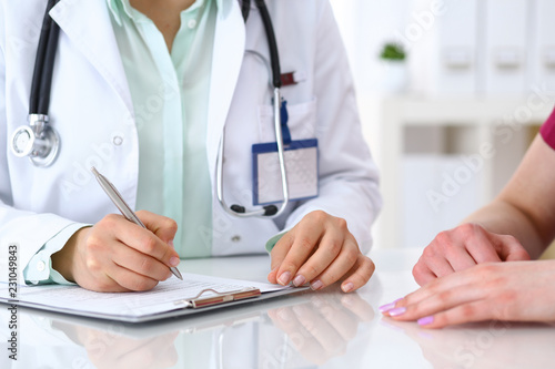 Doctor woman consulting patient while filling up an application form at the desk in hospital. Just hands close-up. Medicine and health care concept