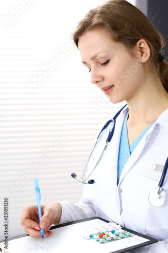 Woman doctor at work at hospital. Young female physician write prescription or filling up medical form while sitting in hospital office