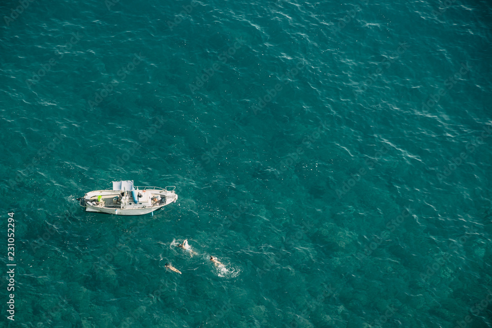 Aerial view on small boat on open waters with people swimming