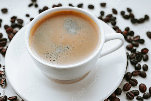 White cup with fresh coffee on saucer close up with grains of coffee on white isolated background