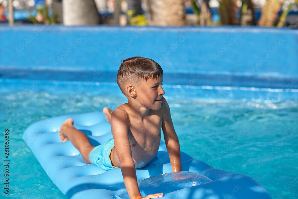 Boy relaxing on inflatable mattress at hotel swimming pool in summer.