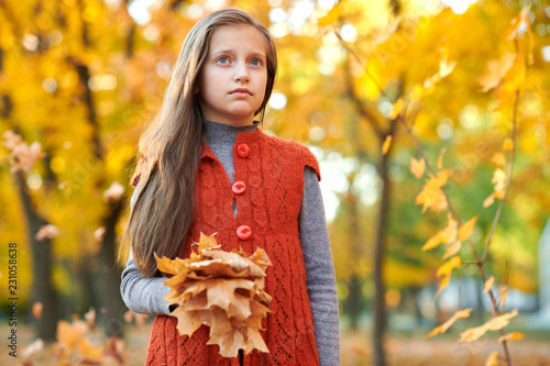 Girl child with yellow leaves is in autumn city park. Bright yellow trees.