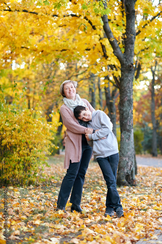 Mother and son are in autumn city park. They are parents posing, smiling, playing and having fun. Bright yellow trees.