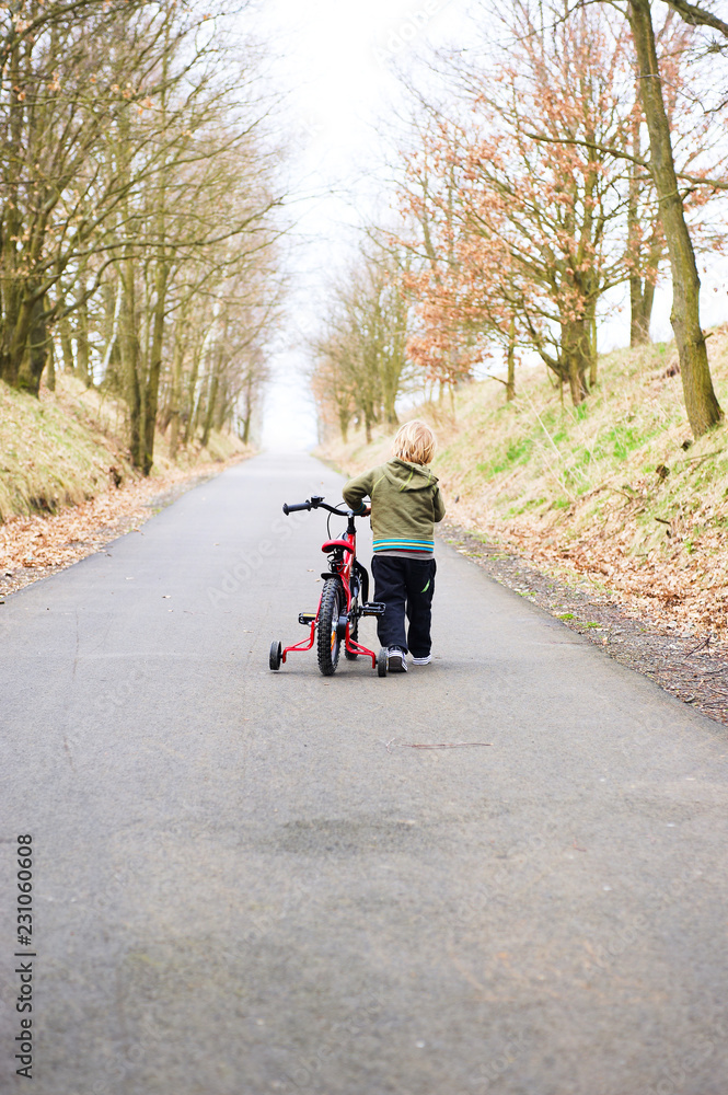 Little child boy on bicycle in park outdoor. A child is riding a children's bike with training support wheels Little child boy on bicycle in park outdoor. A child is riding a children's bike with training support wheels