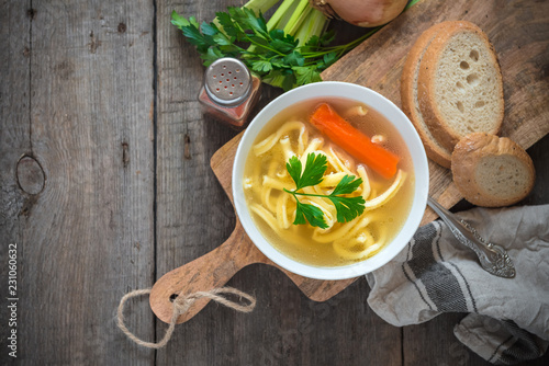 Chicken soup with noodles and carrot in white bowl.
