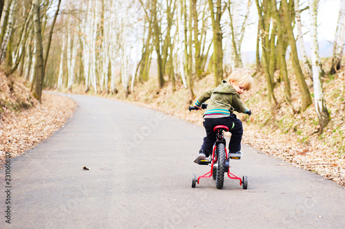 Little child boy on bicycle in park outdoor. A child is riding a children's bike with training support wheels 