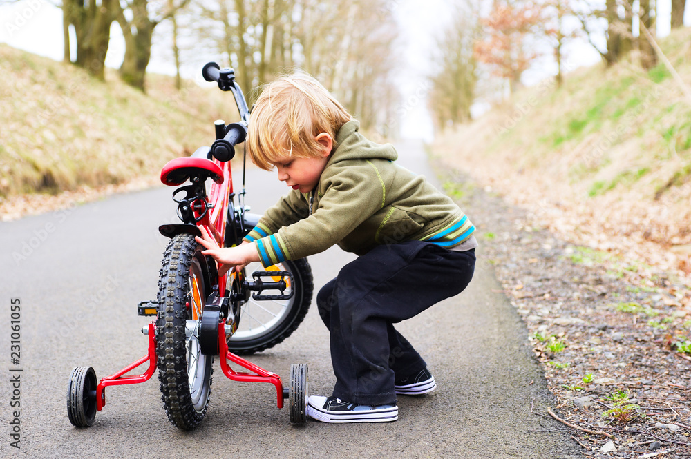 Obraz premium Little child boy on bicycle in park outdoor. A child is riding a children's bike with training support wheels 